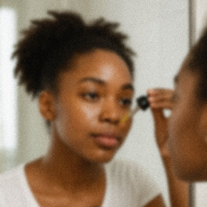 A woman pressing serum from a dropper onto her cheek